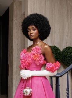 a woman in a pink dress and white gloves standing on a stair case holding a purse