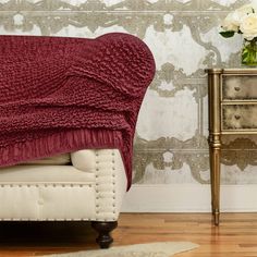 a red blanket sitting on top of a couch next to a vase with white flowers