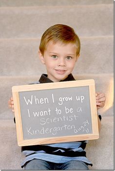 a young boy holding up a sign that says when i grow up i want to be a scientist