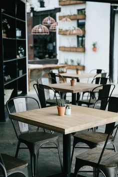 an empty restaurant with tables and chairs in front of the window, filled with potted plants