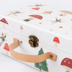 a white box with mushrooms and trees painted on the lid is holding a brown ribbon