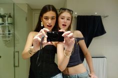 two young women are taking a selfie in front of the bathroom mirror with their cell phone