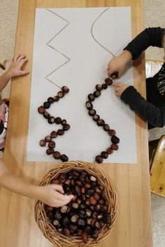 two children are making a bead necklace out of acorns on a table