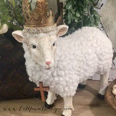 a white sheep with a crown on it's head standing in front of a potted plant