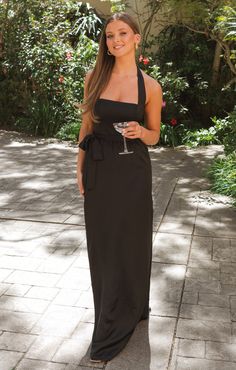 a woman in a black dress is holding a wine glass and posing for the camera