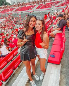 two girls posing for the camera in front of red bleachers at a sporting event