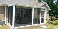 an enclosed patio with chairs and table in front of a brick house on a sunny day