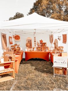 an outdoor market with orange tables and white tents set up in the grass for sale