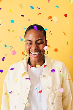 a woman standing in front of a yellow wall with confetti on it