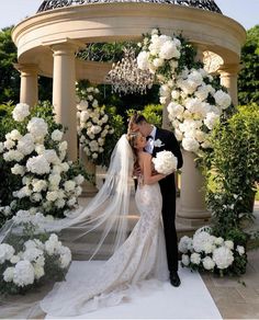 a bride and groom kissing in front of a gazebo with white flowers on it