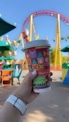 a person holding up a cup in front of an amusement park ride