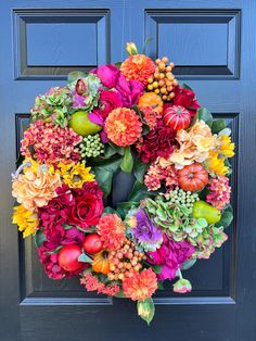 a colorful wreath is hanging on the front door with an apple and flower arrangement in it