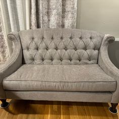 a grey couch sitting on top of a hard wood floor next to a curtained window