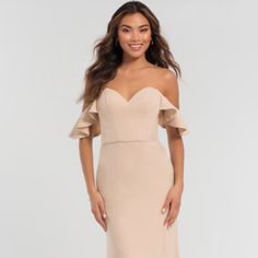 a woman in a nude colored dress with an off the shoulder neckline and ruffled sleeves