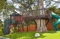 there is a tree house with a slide in the yard and a play area on the other side