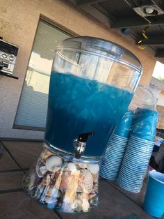 a blue beverage dispenser sitting on top of a table next to cups