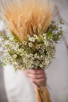 a person holding a bouquet with white flowers and greenery in their hands, while wearing a white shirt