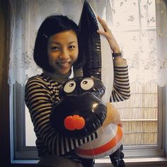 a woman holding up a balloon shaped like a monkey with eyes and nose, while standing in front of a window