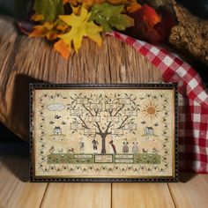 a cross stitch pattern on a wooden table with autumn leaves and fall foliage in the background