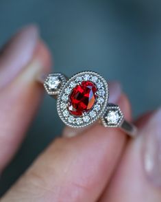 a woman's hand holding a ring with a red stone and diamonds on it