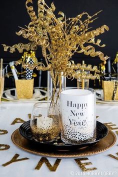 a table topped with glasses and vases filled with gold foiled branches in front of a happy new year sign