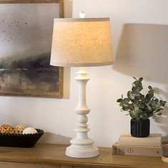 a white lamp sitting on top of a wooden table next to a book and potted plant