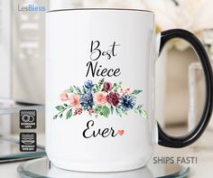 a white coffee mug with the words best niece ever on it and flowers in black lettering