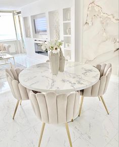 a marble dining table surrounded by chairs and vase with flowers on it in a white living room