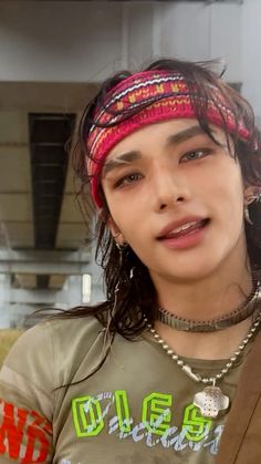 a young man with long hair wearing a bandana and looking at the camera while standing in front of a building