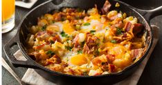 a skillet filled with eggs and bacon on top of a wooden table next to orange juice