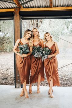 three bridesmaids in brown dresses holding bouquets and smiling at the camera while standing under an awning