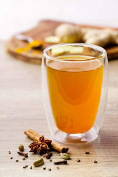 a glass cup filled with liquid next to cinnamon and anise on a wooden table