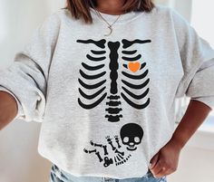 a woman wearing a skeleton sweatshirt with an orange heart in the middle and her hands on her hips