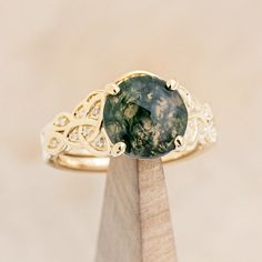 a ring with a green stone in it on top of a piece of wooden stand