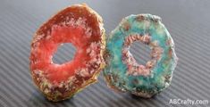 two doughnuts with different colors and designs sitting on top of a table next to each other