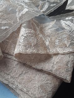 several pieces of silver brocaded fabric on top of each other with flowers and leaves