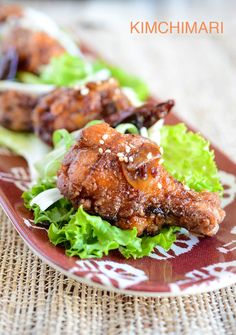 chicken wings with sesame seeds and lettuce are on a red plate that is sitting on a woven tablecloth