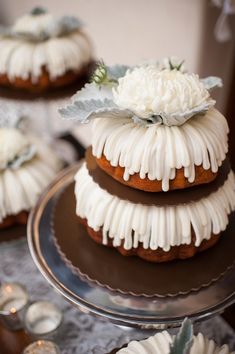 three tiered cake with white frosting and flowers on top, sitting on a plate