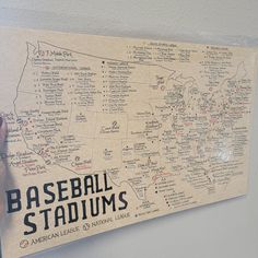 a baseball stadium map hanging on the wall with someone's hand pointing at it