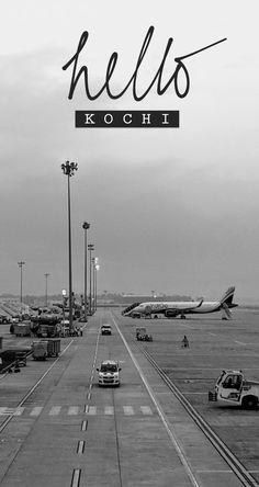 black and white photograph of an airport with cars on the tarmac, planes in the background