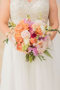 a woman in a wedding dress holding a bouquet of pink, orange and white flowers