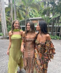 three women standing next to each other on a brick walkway in front of palm trees