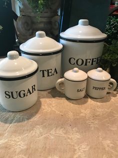 four white coffee canisters sitting on top of a table next to a potted plant