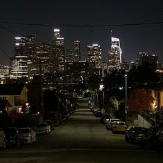 the city skyline is lit up at night, with cars parked on the side of the street