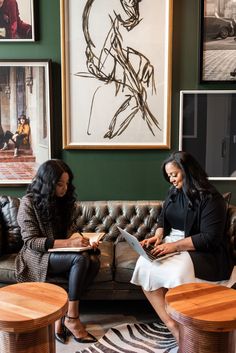 two women sitting on a couch looking at papers