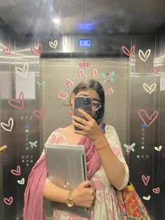 a woman taking a selfie in front of an elevator with hearts on the wall