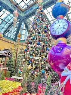 the christmas tree is decorated with many colorful balls and ornaments, as well as a large clock