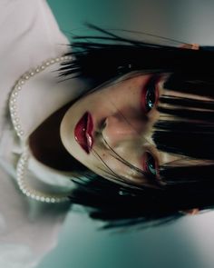 a woman with long black hair and red eyes posing for a photo in white shirt