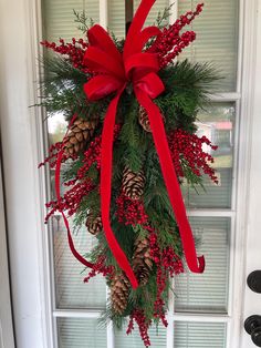 a christmas wreath with pine cones and red ribbon hanging on the front door to welcome guests