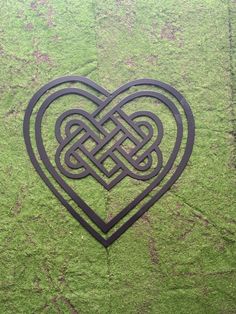 a heart shaped metal object sitting on top of a green grass covered field with an intricate knot in the center